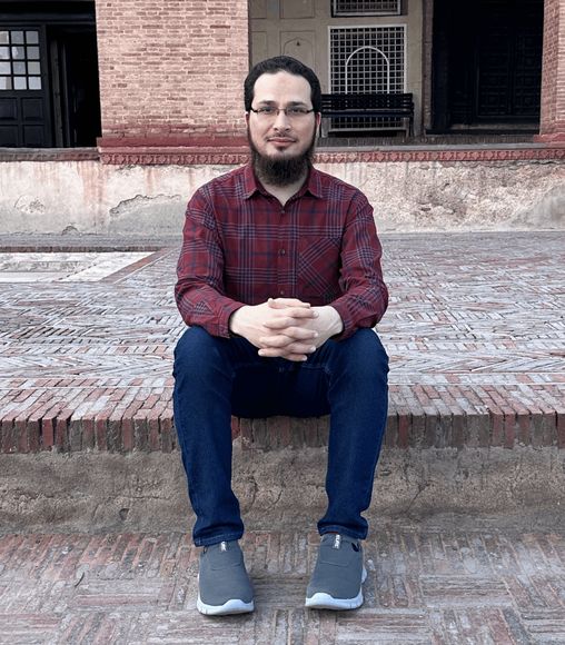 Behzad Hussain seated in a historic brick courtyard in Lahore, Pakistan